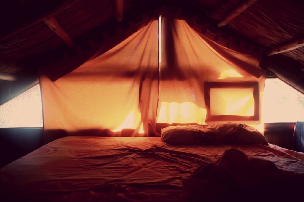 Egy megnyugtató kép, egy barna ágy a tetőtérben, az ablak letakarva egy barna függönnyel.